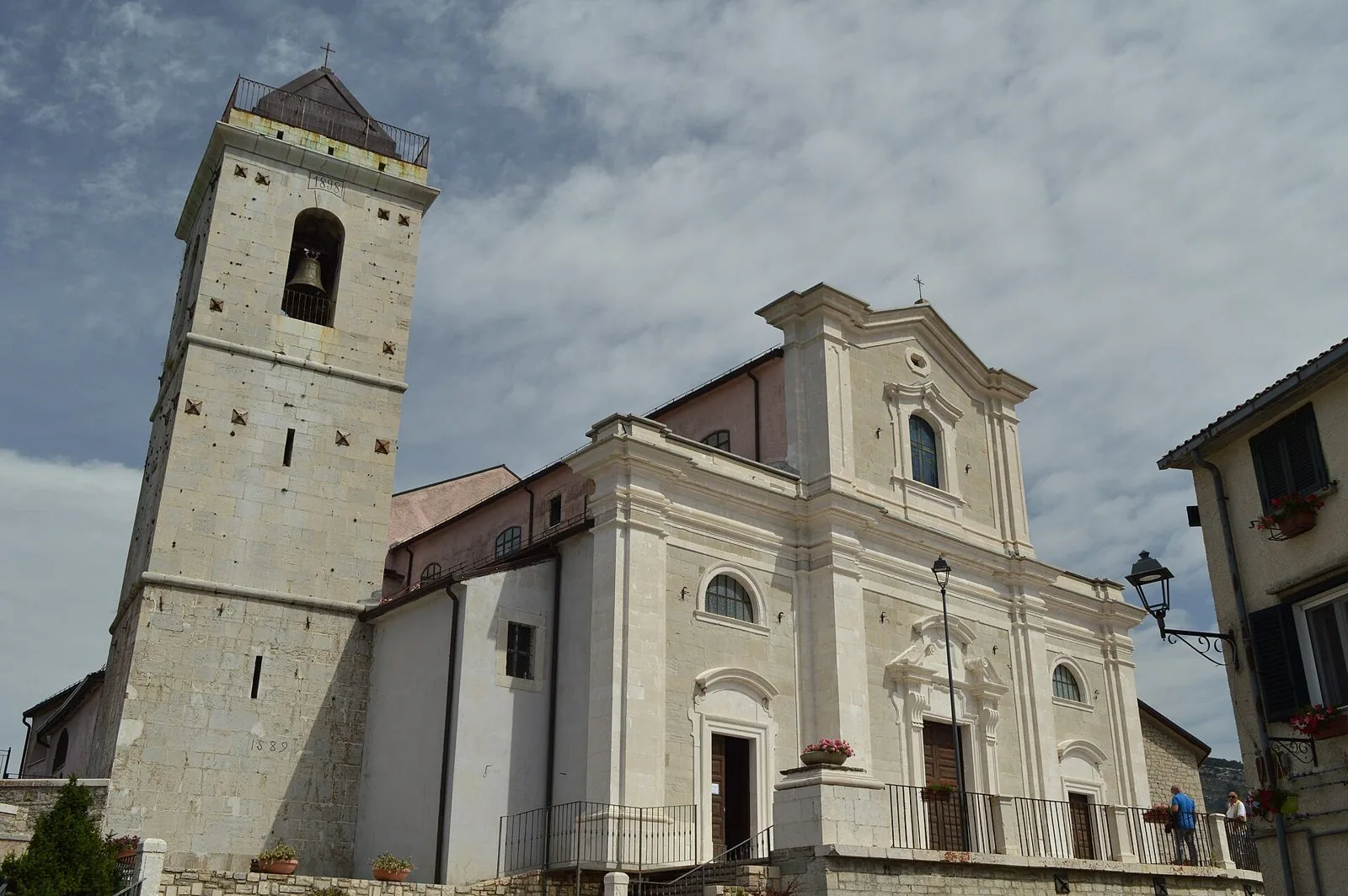 Facciata in pietra chiara e campanile della chiesa madre di Santa Maria Assunta a Capracotta sotto un cielo estivo